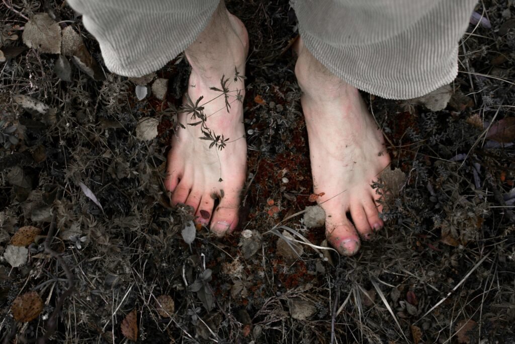 Close-up of bare feet on earthy and natural ground covered in foliage.